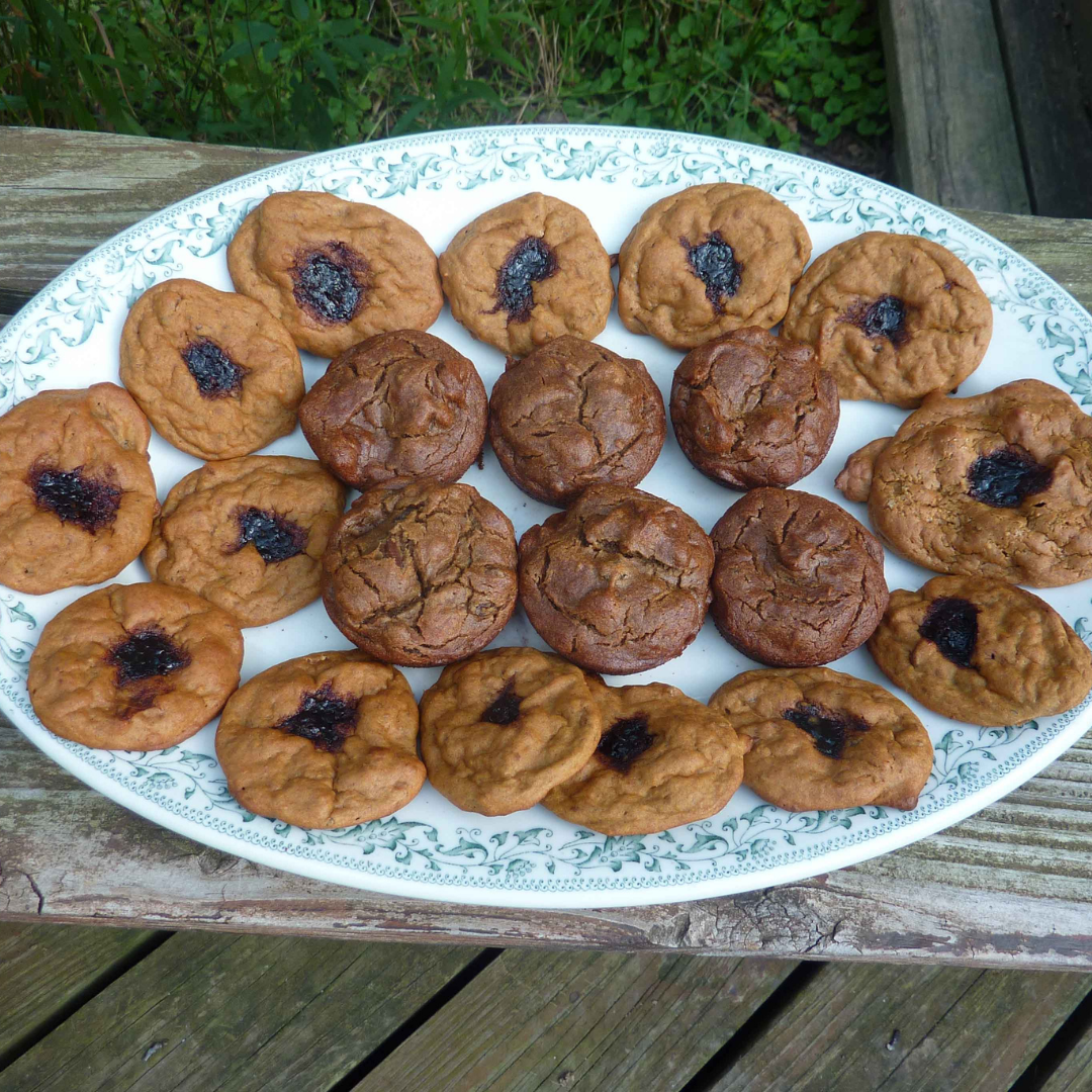 A plate of tan/orange cookies with deep purple jam in the center